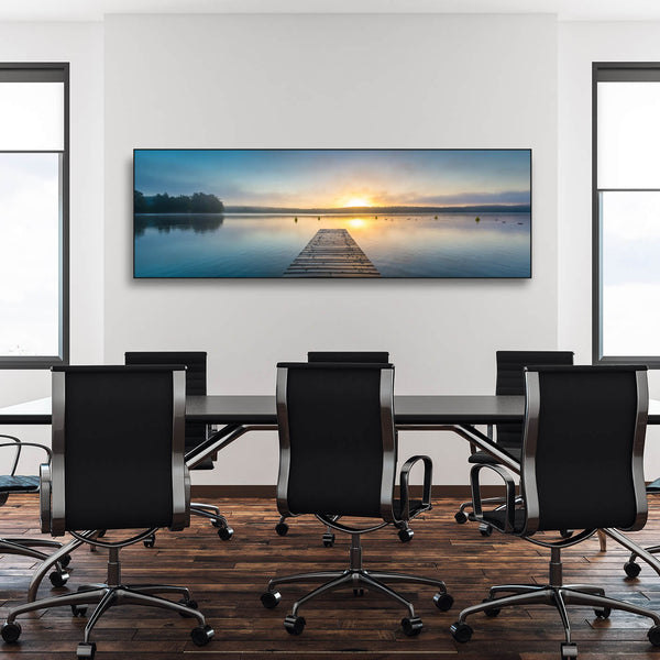 Konferenzraum mit langem Tisch, Bürostühlen und Schallschutzbild mit Bootssteg im See bei Sonnenaufgang. Schwarzer Rahmen im Querformat.