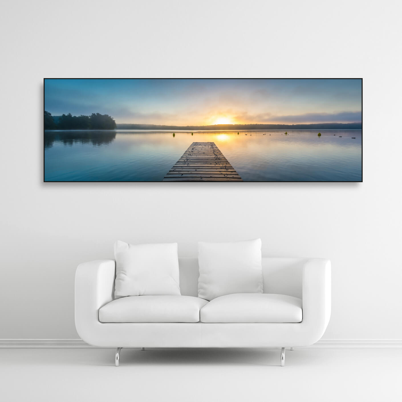 Schallschutzbild mit Bootssteg im See bei Sonnenaufgang. Schwarzer Rahmen im Querformat über weißem Sofa.