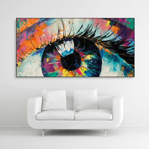 Schallschutzbild mit dick aufgetragener Farbe gemaltes, abstraktes Auge in bunten Farbtönen. Schwarzer Rahmen in Querformat 2 zu 1 über weißem Sofa.