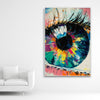 Schallschutzbild mit dick aufgetragener Farbe gemaltes, abstraktes Auge in bunten Farbtönen. Weißer Rahmen im Hochformat neben weißem Sofa.