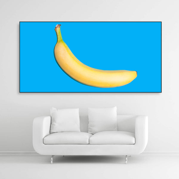 Tysta Akustikbild mit Fotografie einer gelben Banane auf hellblauen Hintergrund. Schwarzer Rahmen im Querformat 2 zu 1 über weißem Sofa.