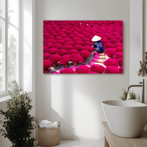 Eine große Fotografie hängt an einer Wand in einem hellen Badezimmer. Das Bild zeigt eine weite Fläche mit leuchtend roten Blumen. In der Mitte sitzt eine Person mit einem traditionellen Strohhut und arbeitet an den Blumen. Das Badezimmer ist modern eingerichtet mit einer freistehenden Badewanne und einem Korb mit Handtüchern.