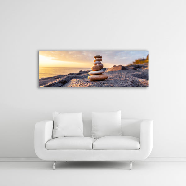 Ein Panorama-Wandbild mit einem Stapel aus gestapelten Steinen am Strand bei Sonnenuntergang.