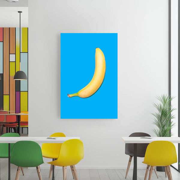 Ein leuchtend gelbes Bananenmotiv hängt an einer weißen Wand in einem modernen Essbereich. Der Raum ist hell und freundlich mit bunten Akzenten wie gelben Stühlen und einem bunten Wanddekor.