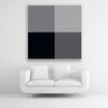 Tysta Akustikbild Colorline Black mit vier Vollfarben Schwarz und Grau. Weißer Bilderrahmen im Quadrat über weißem Sofa.