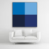 Tysta Akustikbild Colorline Blue mit vier Vollfarben aus Blautönen. Schwarzer Bilderrahmen im Quadrat über weißem Sofa.
