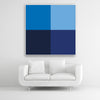 Tysta Akustikbild Colorline Blue mit vier Vollfarben aus Blautönen. Weißer Bilderrahmen im Quadrat über weißem Sofa.
