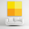 Tysta Akustikbild Colorline Yellow mit vier Vollfarben aus Gelbtönen. Weißer Bilderrahmen im Quadrat über weißem Sofa.