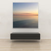 Akustikbild Silent Ocean 2 von Tan Kulali mit abstraktem Meerblick bei Sonnenuntergang. Quadratisch mit weißem Rahmen über Sitzbank.