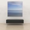 Akustikbild Silent Ocean 4 von Tan Kulali mit abstraktem Meereshorizont in Blautönen. Quadratisch mit weißem Rahmen über Sitzbank.